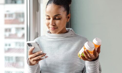 young woman holding medications, looking on phone