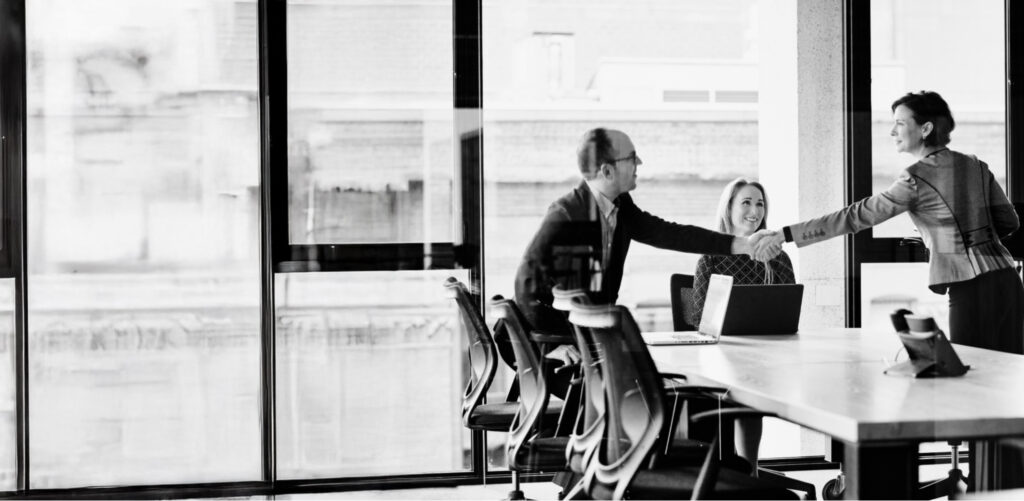 Professional man and woman shaking hands during a business meeting with a third colleague, representing trust and collaboration in clinical trials at YPrime.