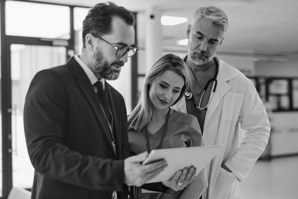 Clinical research professionals, including a man and woman with stethoscopes, being guided by a business professional reviewing eCOA data on a tablet, symbolizing collaboration, data integrity, and operational excellence in clinical trials, with relevance to YPrime’s eCOA solutions for CROs.