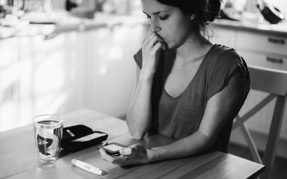 A woman looks concerned while checking her Type 1 Diabetes monitor, illustrating the mental health challenges associated with managing chronic conditions—an area of focus in clinical research and digital health solutions.