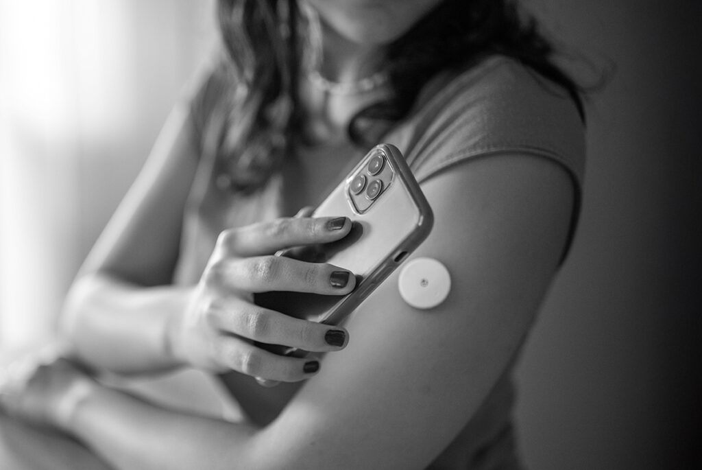 Woman using a smartphone app to check glucose levels from a connected monitor on her arm.