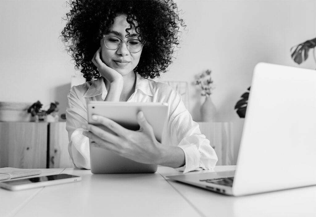 Professional woman at desk reviewing clinical trial IRT system on tablet with laptop and phone nearby, representing technology challenges and solutions for sponsors