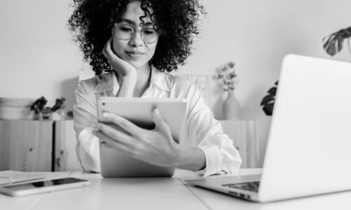 Professional woman at desk reviewing clinical trial IRT system on tablet with laptop and phone nearby, representing technology challenges and solutions for sponsors
