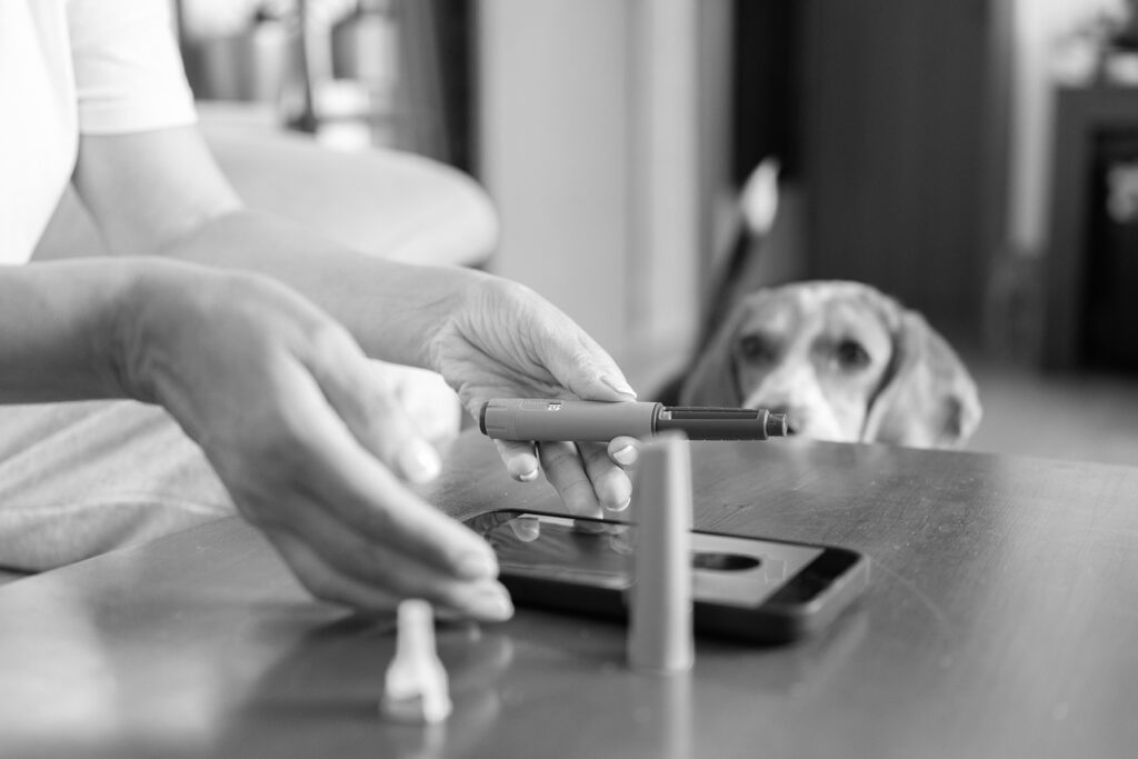 Woman demonstrating semaglutide pen injection for weight loss during a video consultation with a doctor on her mobile phone, with her dog watching