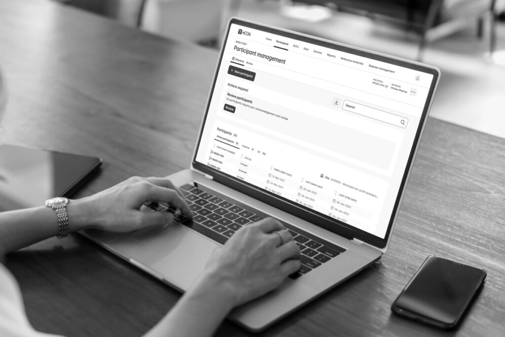 Clinical researcher typing on laptop showing YPrime Advanced eCOA Oversight project management interface for investigator review and sign-off.